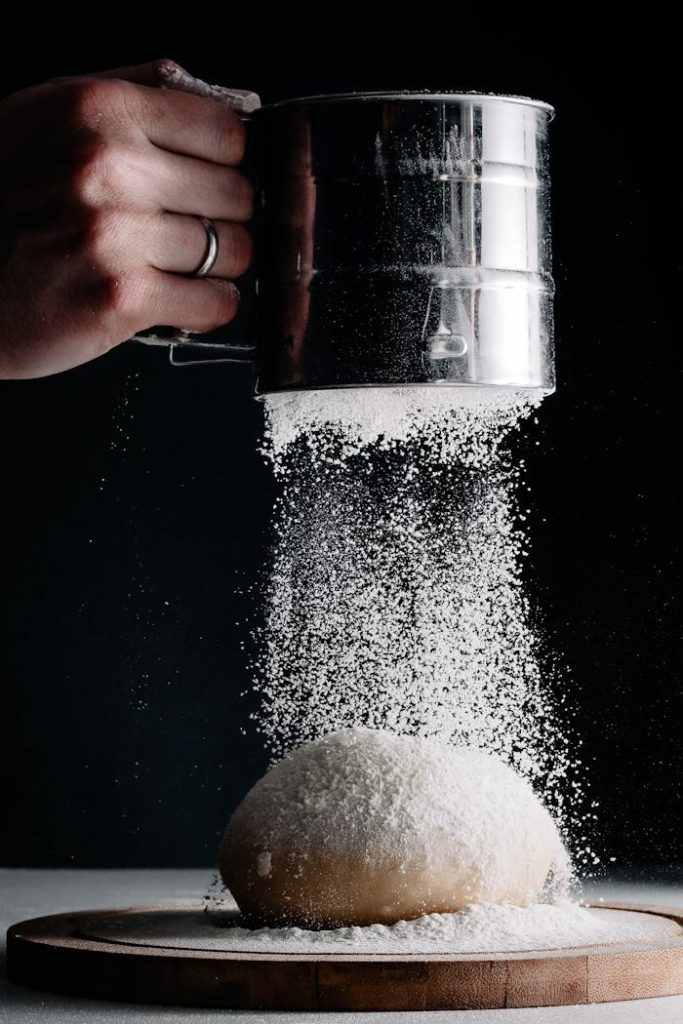 A close-up of flour being sifted over dough, perfect for baking themes.