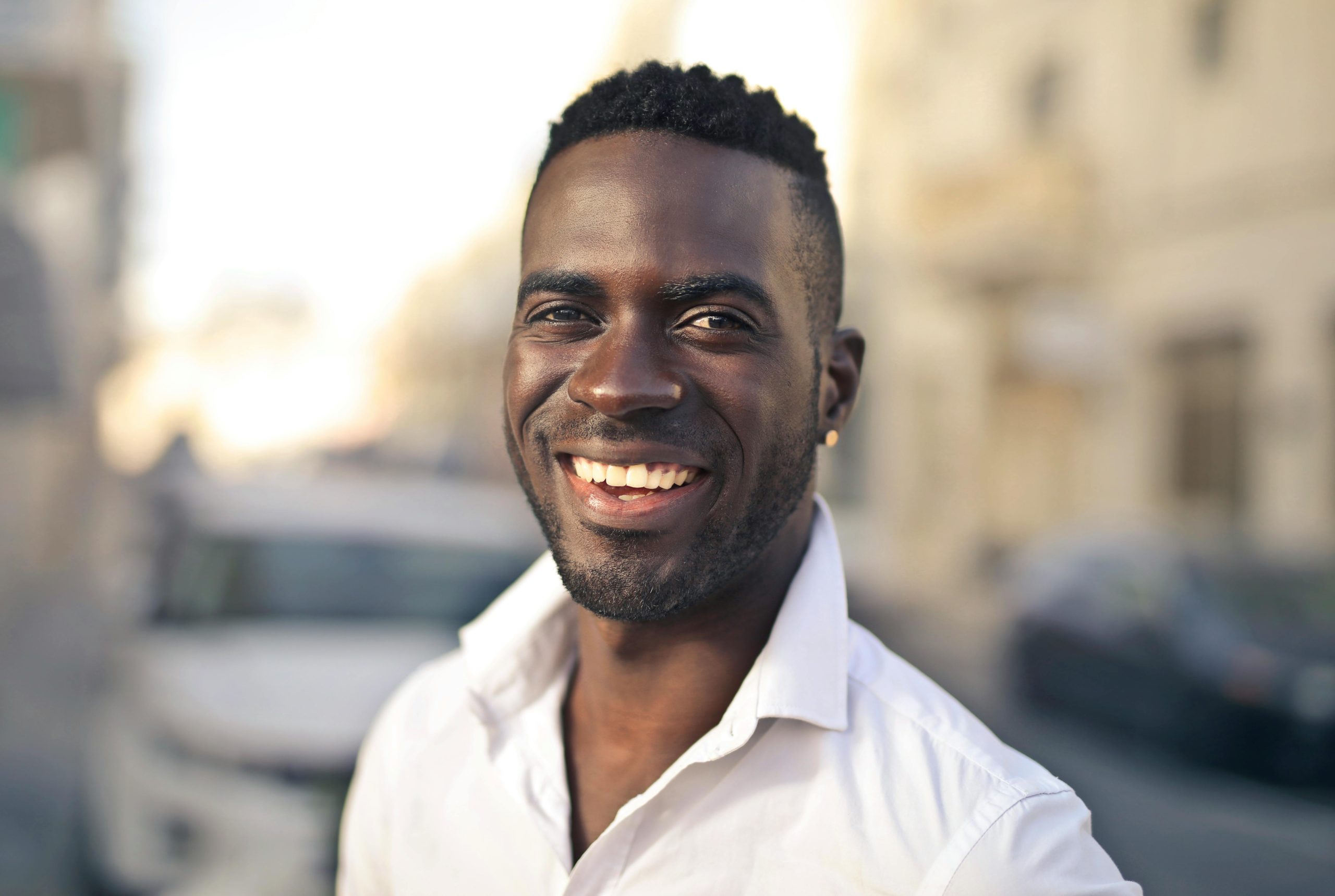 Portrait of a smiling man in a white shirt standing outdoors on a sunny day.