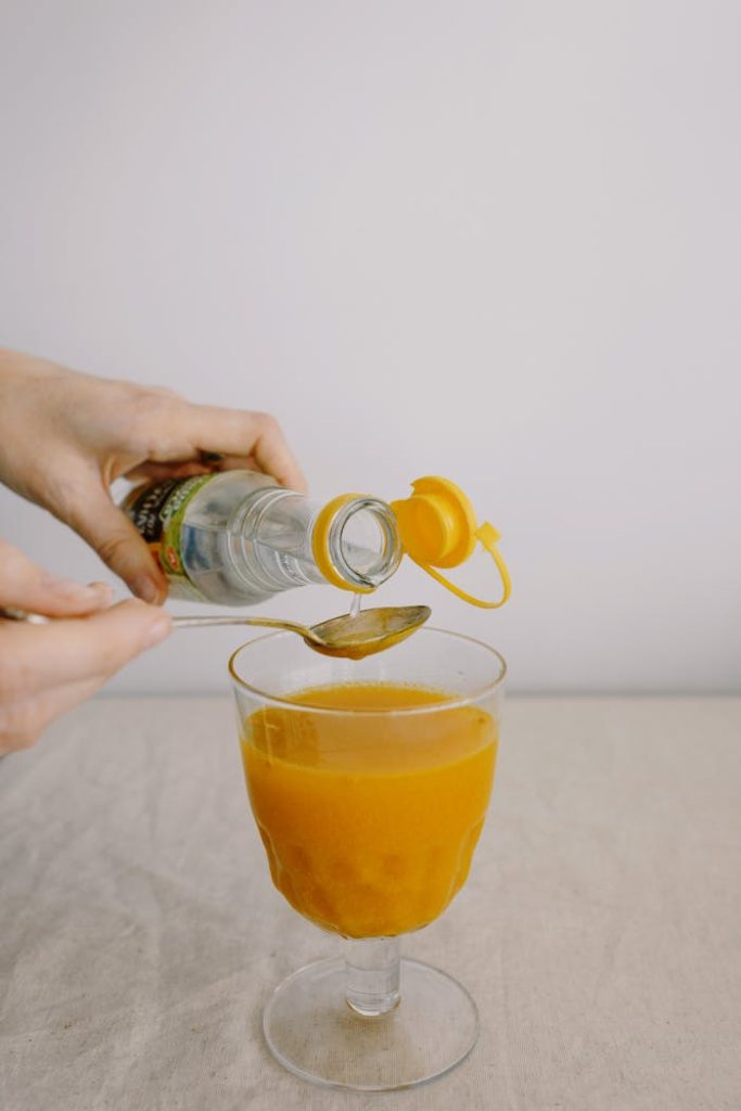 A person pouring vinegar into a goblet of orange juice with a spoon.
