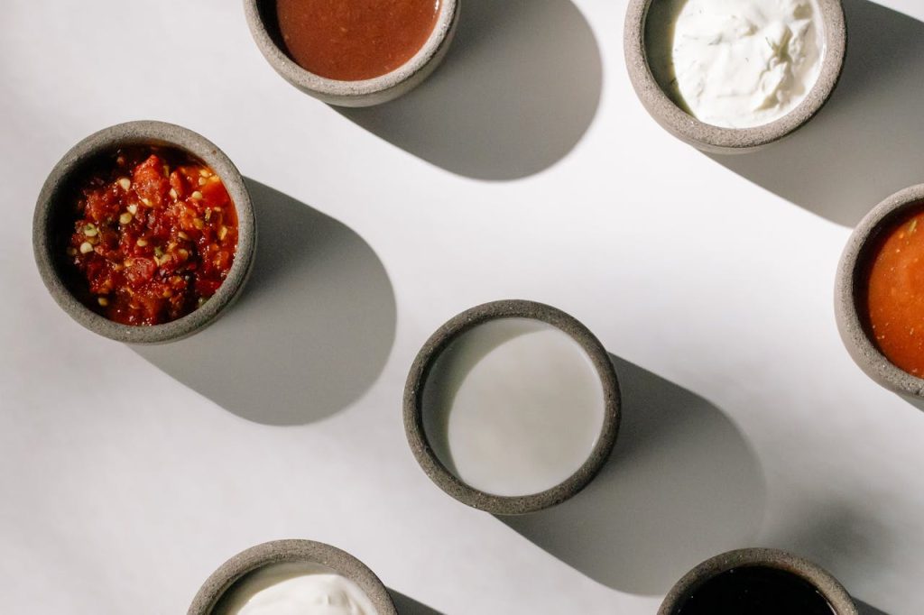 Top view of bowls with various sauces and dips casting shadows on a white surface.
